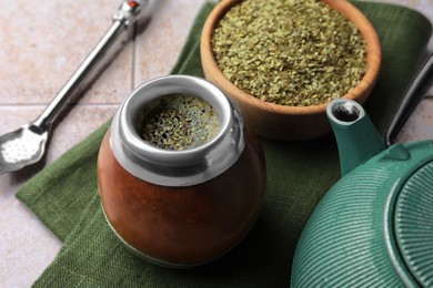 Photo of Calabash, bombilla, bowl of mate tea leaves and teapot on tiled table, closeup