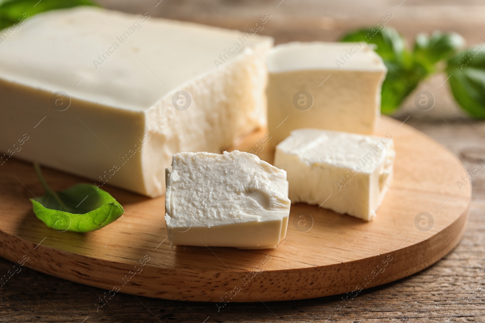 Photo of Board with feta cheese and basil on wooden table, closeup