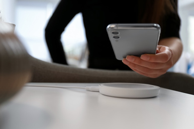 Photo of Woman putting smartphone on wireless charger in room, closeup