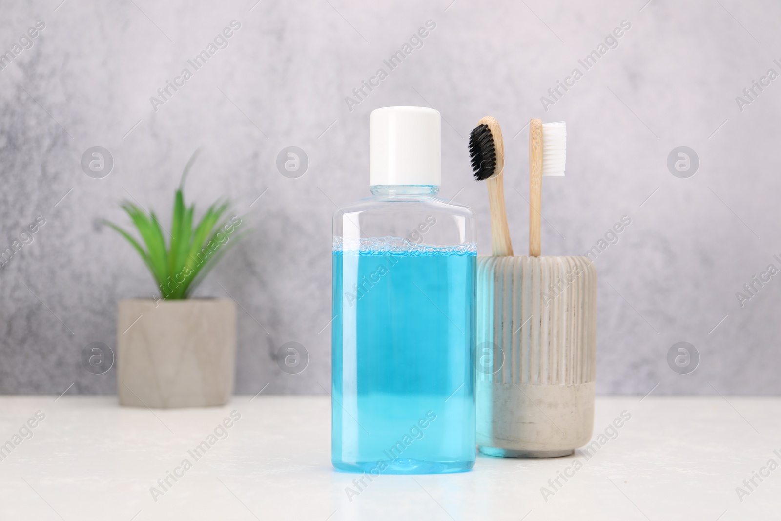 Photo of Bottle of mouthwash and toothbrushes on white table in bathroom