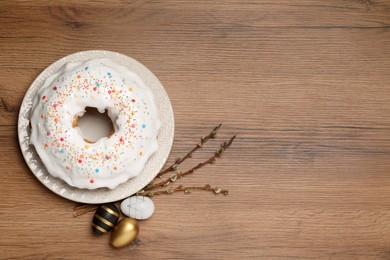 Photo of Easter cake with sprinkles, painted eggs and willow branches on wooden table, flat lay. Space for text