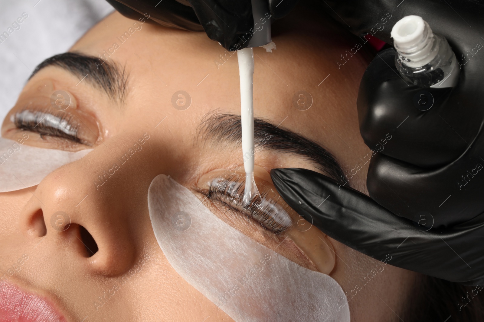 Photo of Young woman undergoing eyelash lamination, closeup. Professional service