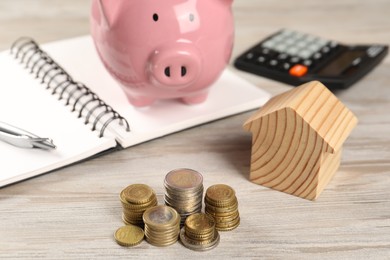 House model, piggy bank, stacked coins, notebook and calculator on wooden table, selective focus