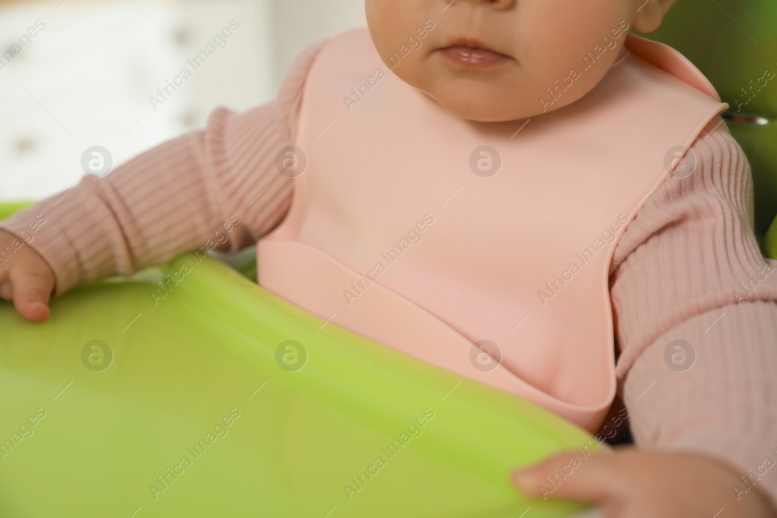 Photo of Cute little baby wearing bib in highchair indoors, closeup