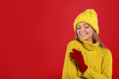 Photo of Young woman in warm sweater, gloves and hat on red background, space for text. Winter season