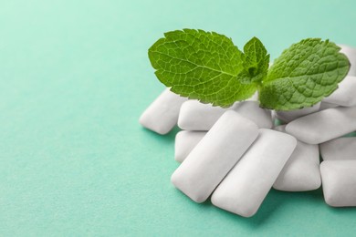 Photo of Tasty white chewing gums and mint leaves on turquoise background, closeup. Space for text