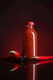 Spicy chili sauce in bottle and peppers against dark background