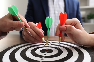 Photo of Business targeting concept. People with darts aiming at dartboard at table indoors, closeup