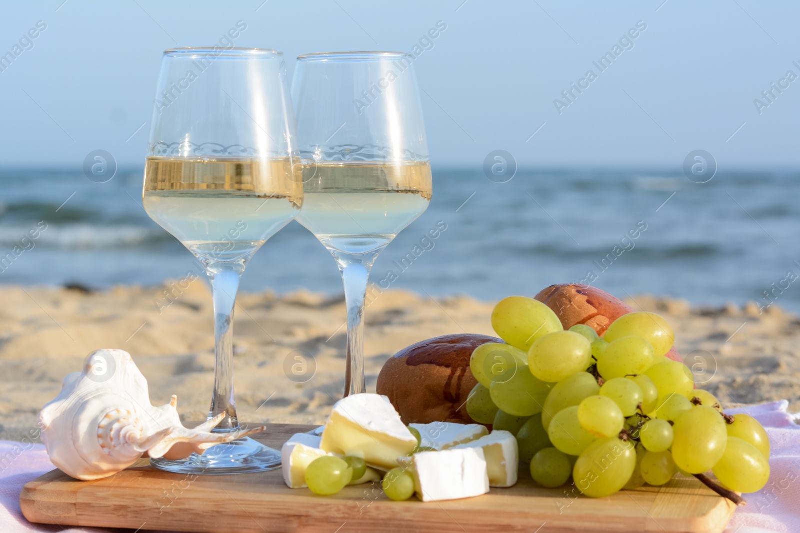 Photo of Glasses with white wine and snacks for beach picnic on sandy seashore