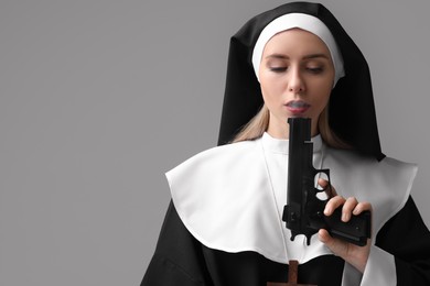Photo of Woman in nun habit holding handgun on grey background. Space for text