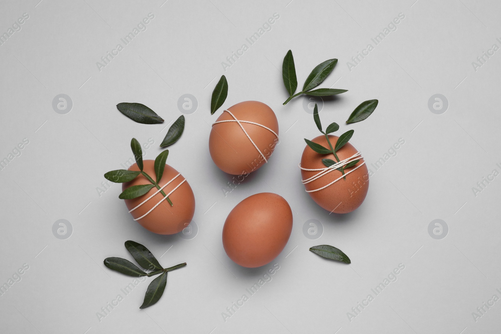 Photo of Beautifully decorated Easter eggs and green leaves on light grey background, flat lay