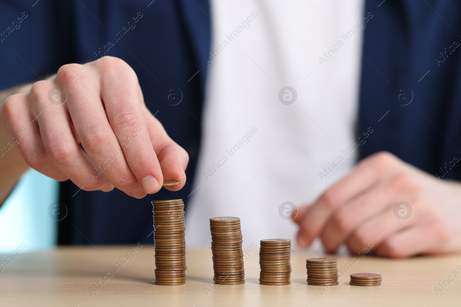 Photo of Financial savings. Man stacking coins at wooden table, closeup