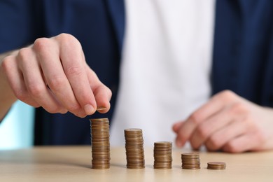 Photo of Financial savings. Man stacking coins at wooden table, closeup