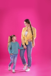 Happy woman and daughter in stylish clothes on color background