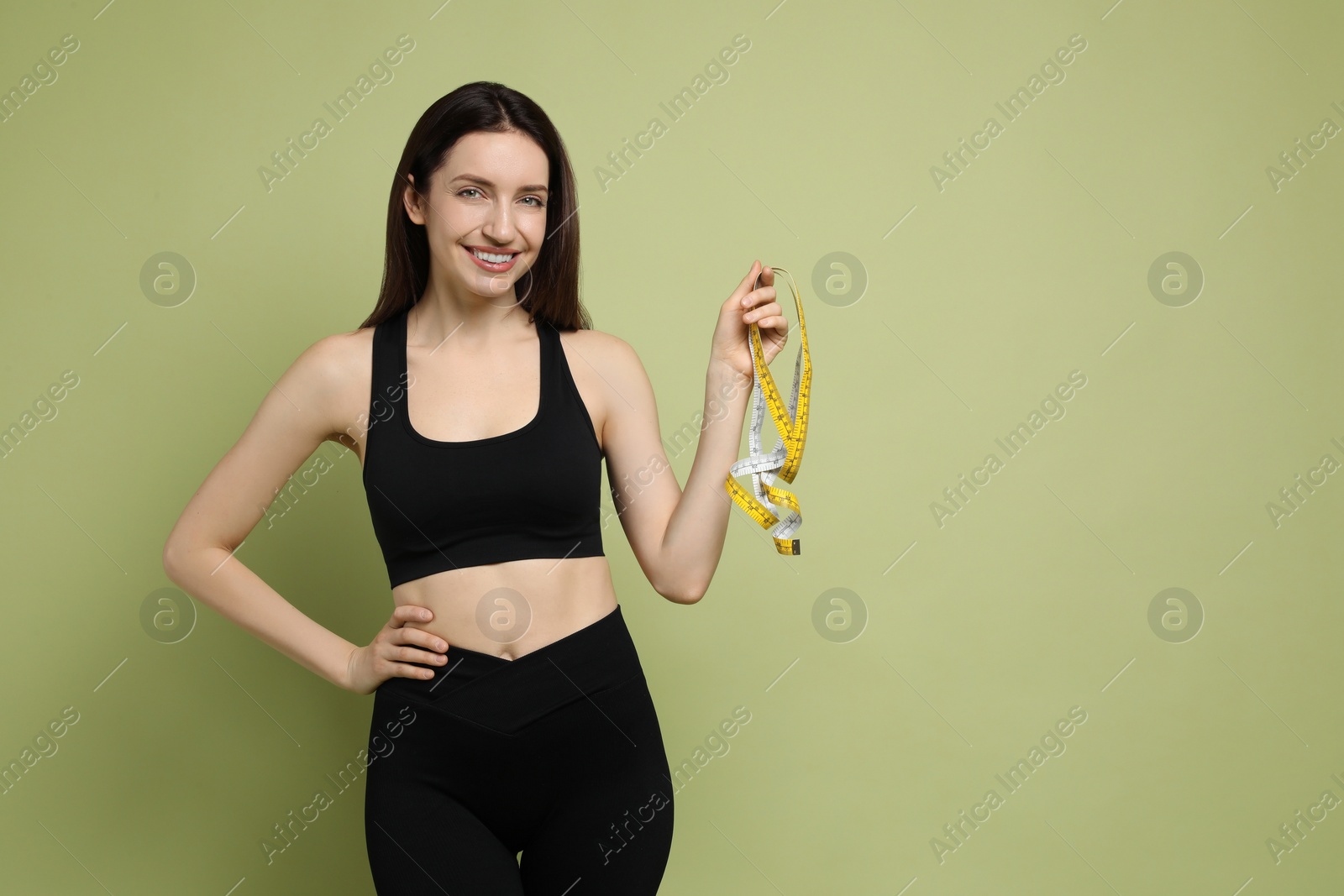 Photo of Happy young woman with measuring tape showing her slim body on green background, space for text