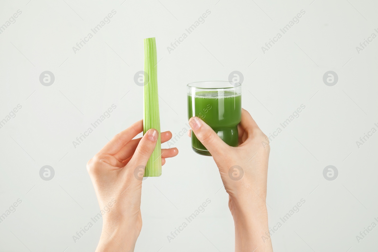 Photo of Woman holding glass of delicious celery juice and fresh vegetable on light grey background, closeup