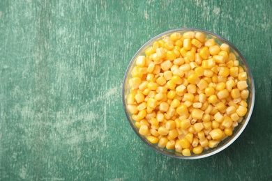 Photo of Bowl with corn kernels on green wooden background, top view. Space for text