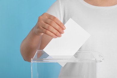 Photo of Woman putting her vote into ballot box on light blue background, closeup