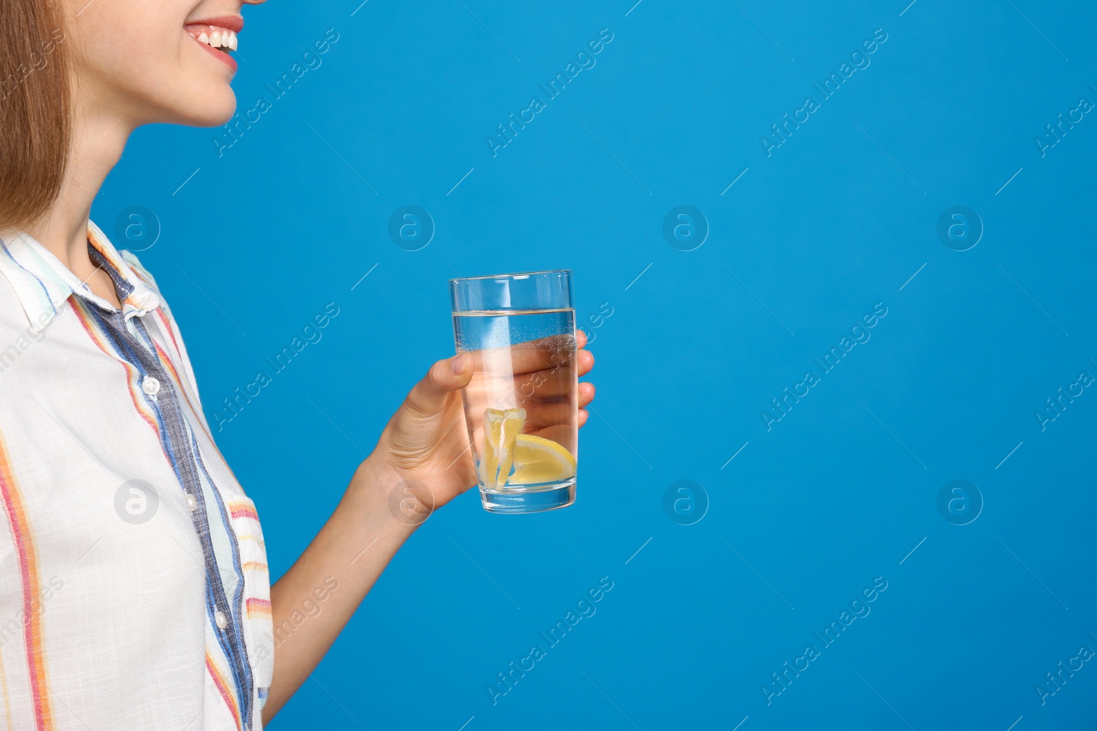 Photo of Young woman with glass of lemon water on light blue background, closeup. Space for text