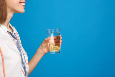 Young woman with glass of lemon water on light blue background, closeup. Space for text