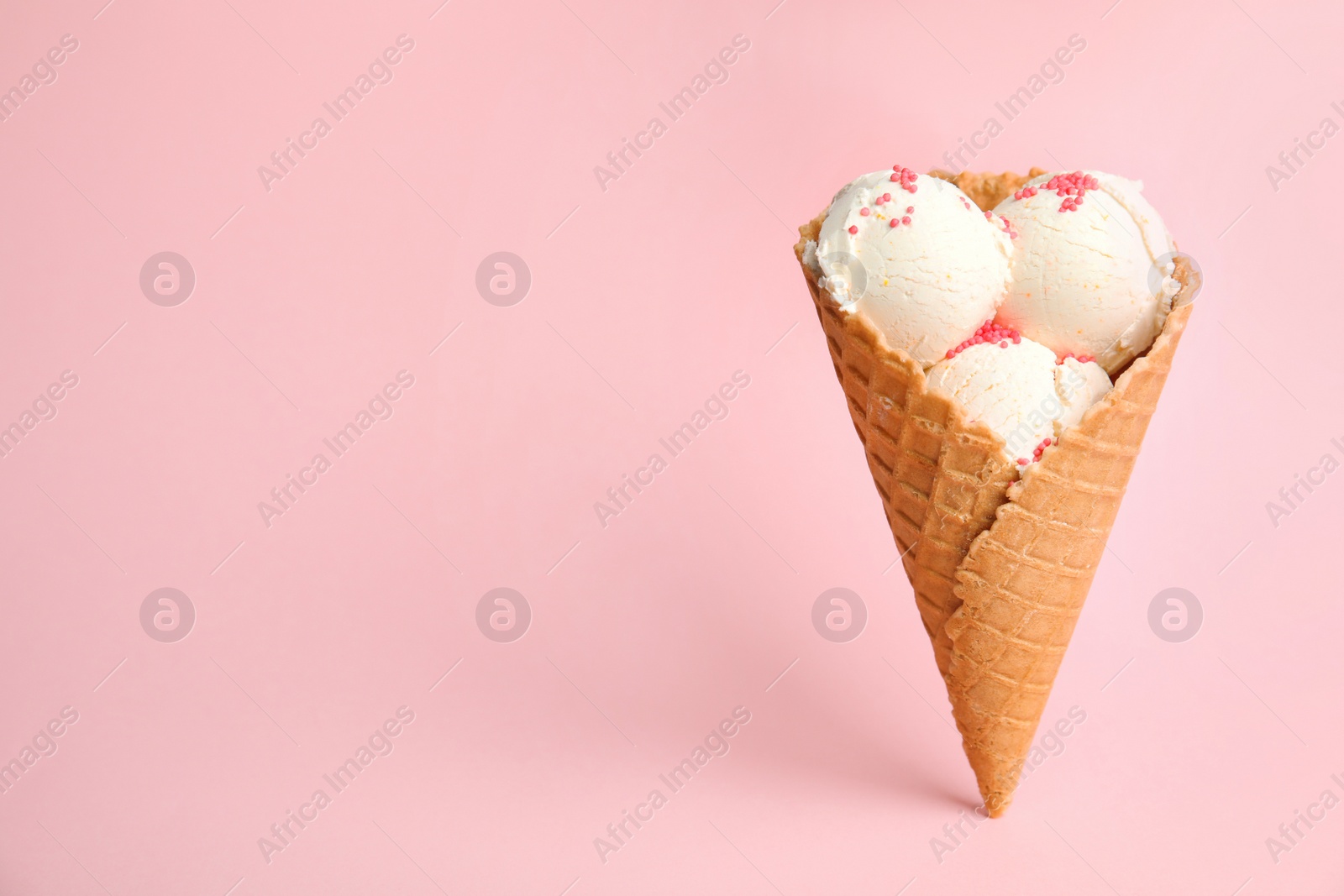 Photo of Delicious vanilla ice cream in wafer cone on pink background. Space for text