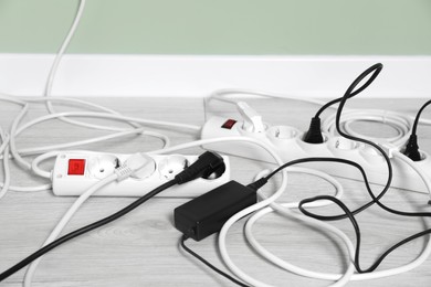 Photo of Power strips with different electrical plugs on white floor indoors, closeup