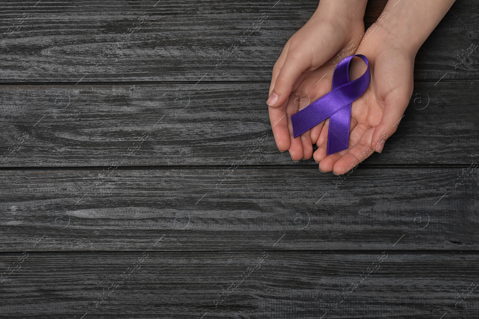 Photo of Woman holding purple awareness ribbon on black wooden background, top view with space for text