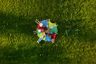 Image of Group of children with teachers holding hands together on rainbow playground parachute in park, top view. Summer camp activity