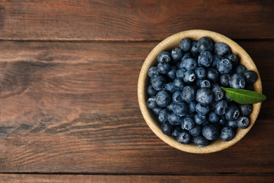 Photo of Tasty ripe blueberries in bowl on wooden table, top view. Space for text