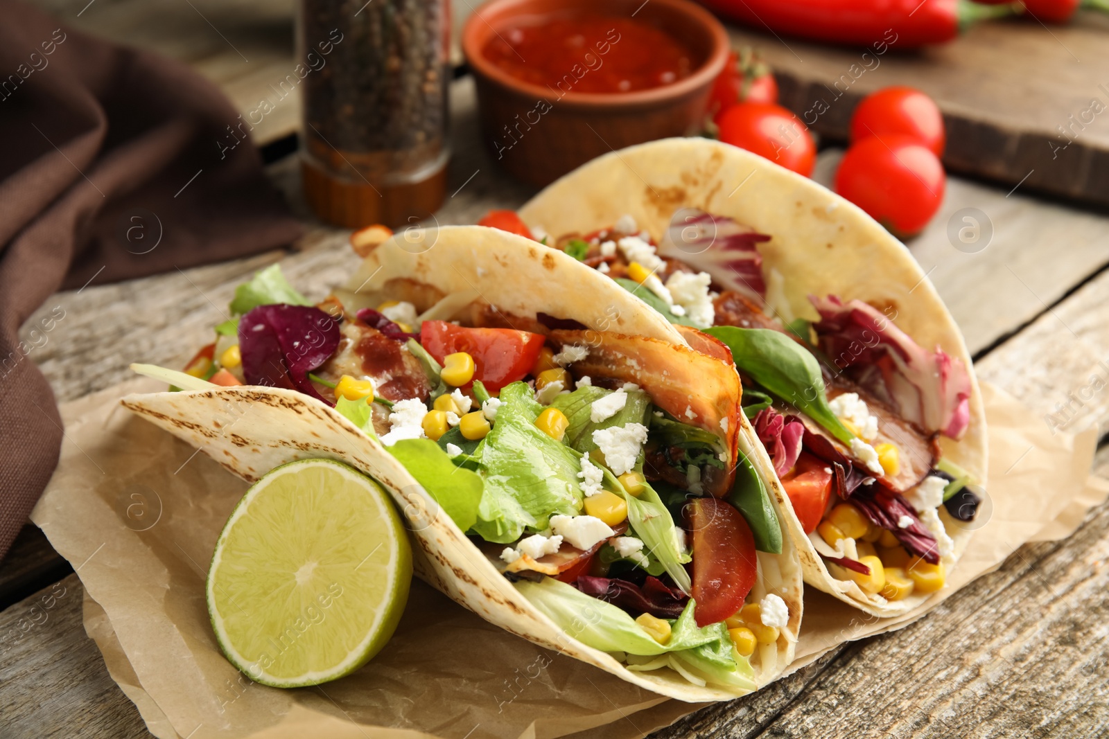 Photo of Delicious tacos with fried bacon and lime on wooden table, closeup