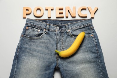 Photo of Men jeans with banana and word Potency made of wooden letters on light grey background, flat lay