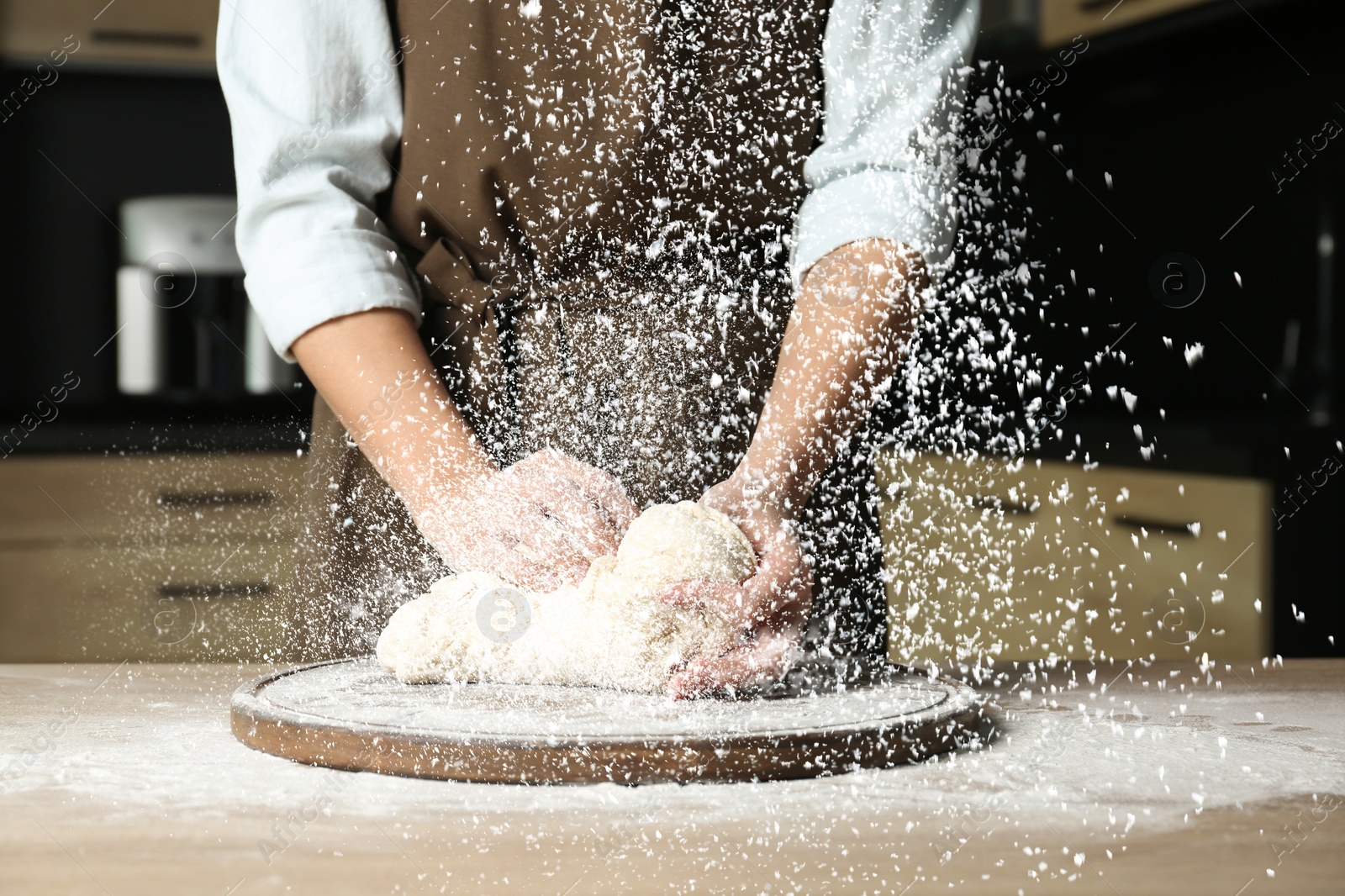 Image of Young woman kneading dough at table in kitchen, closeup