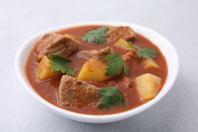 Photo of Delicious goulash in bowl on light grey table, closeup