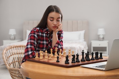 Photo of Thoughtful young woman playing chess with partner through online video chat at home