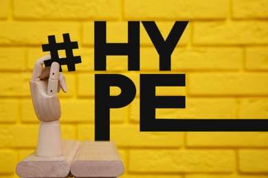 Word Hype near wooden mannequin hand with paper hashtag symbol against yellow brick wall