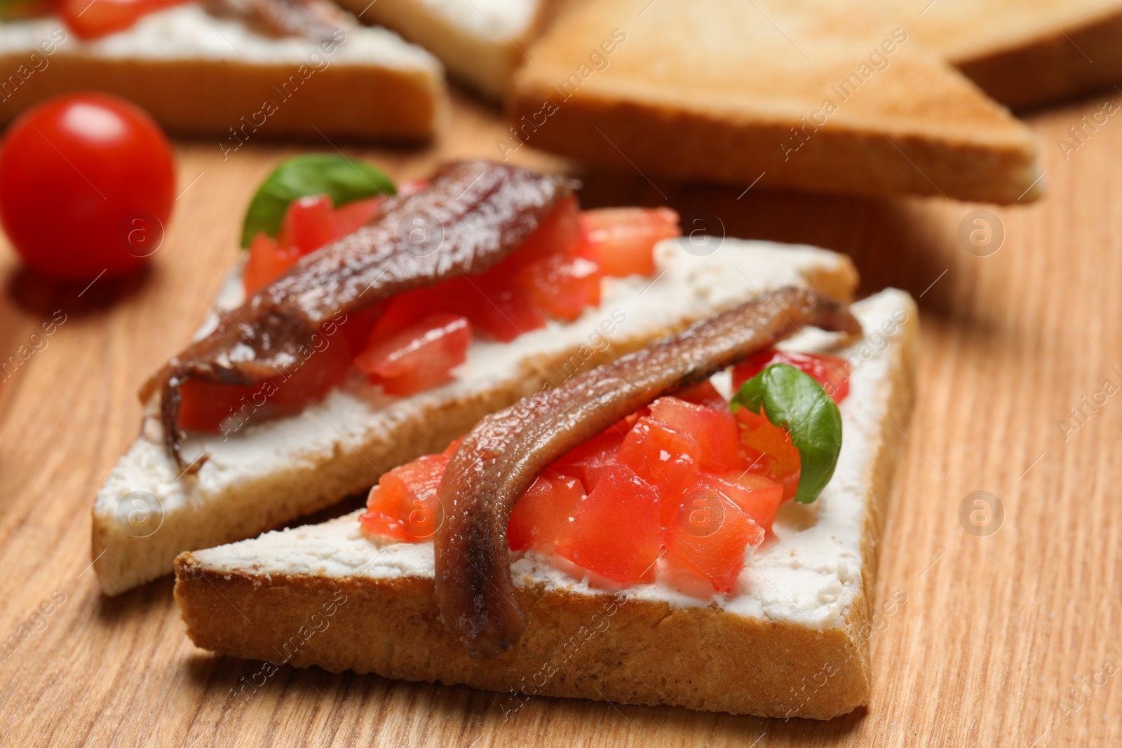 Photo of Delicious sandwiches with cream cheese, anchovies, tomatoes and basil on wooden board, closeup