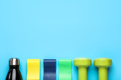 Photo of Set of fitness elastic bands, dumbbells and water bottle on light blue background, flat lay. Space for text