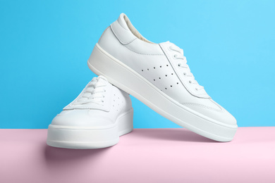 Stylish white shoes on pink paper against light blue background