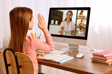 Image of E-learning. Little girl raising her hand to answer during online lesson at wooden table indoors