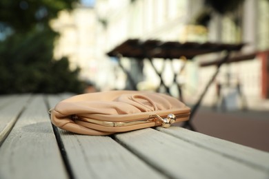 Photo of Beige leather purse on wooden bench outdoors, space for text. Lost and found