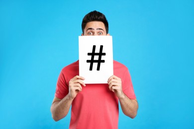 Image of Young man holding paper with hashtag sign on light blue background