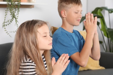 Photo of Children with clasped hands praying on sofa at home