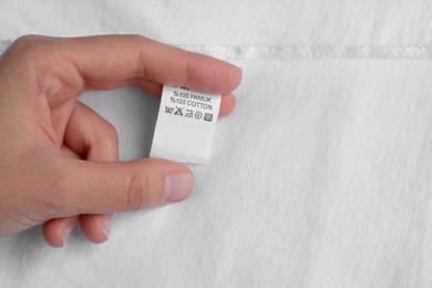 Woman holding clothing label on white garment, top view. Space for text