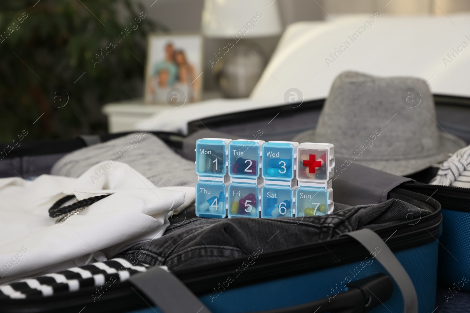 Photo of Open suitcase with packed clothes, accessories and pill box indoors, closeup