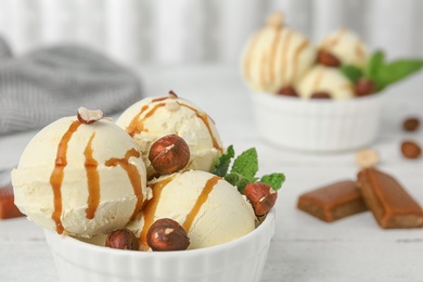 Photo of Delicious ice cream with caramel sauce and hazelnuts served on table, closeup. Space for text
