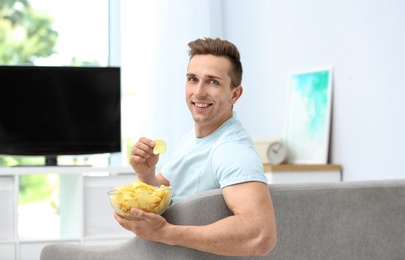 Photo of Man eating potato chips while watching TV in living room