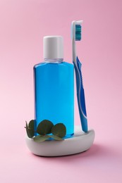 Fresh mouthwash in bottle and toothbrush on pink background