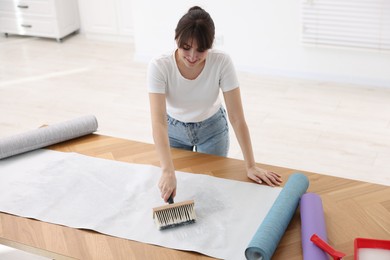 Photo of Woman applying glue onto wallpaper sheet at wooden table indoors