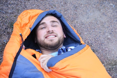 Male camper lying in sleeping bag on ground, view from above