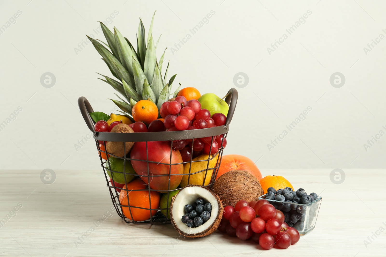 Photo of Metal basket with different fresh fruits on white wooden table
